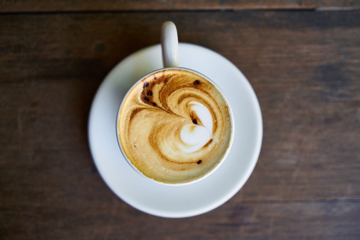 Caffelatte med latte art og et glas te på rustikt bord