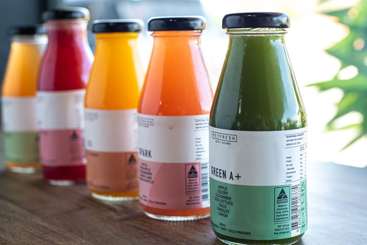 Friskpresset juice i højt glas med appelsin og grønt på bordet